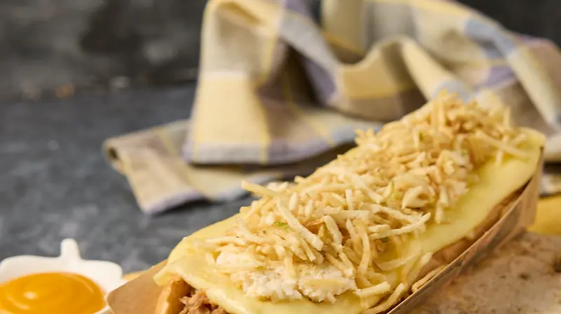 Perro grande con queso fundido y ripio de papa, visto de cerca
