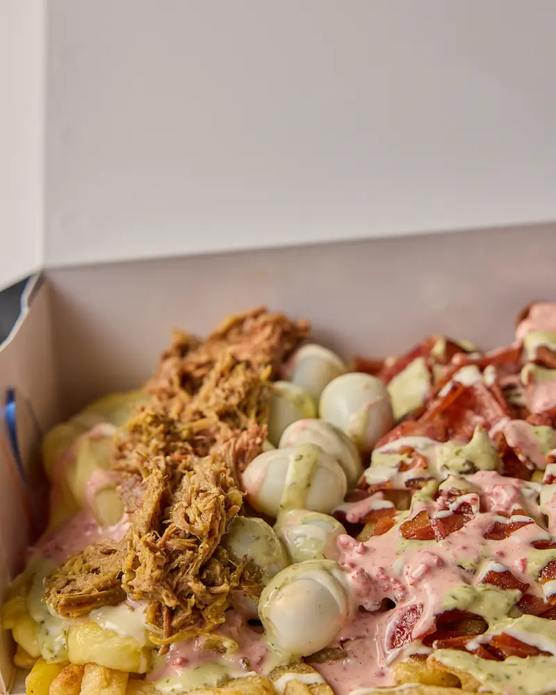 Salchipapas con tocineta, carne desmechada y salsas de la casa